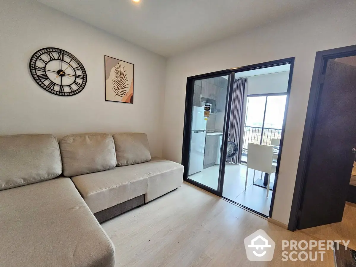 Spacious living room with modern decor, large comfortable sofa, and sliding doors leading to a sunny balcony with outdoor seating.