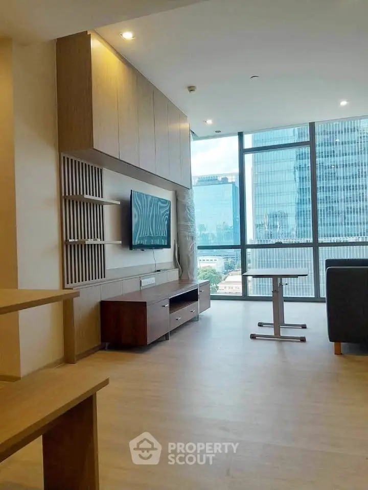 Modern living room with large windows offering stunning city views, featuring sleek furniture and wooden flooring.