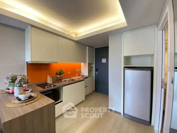 Modern kitchen with sleek cabinetry and vibrant orange backsplash in a stylish apartment.