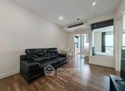 Modern living room with sleek black leather sofa and wooden flooring, leading to a bright bedroom with city views.