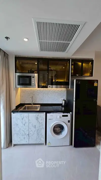 Modern kitchen with washing machine, microwave, and sleek cabinetry in a compact layout.