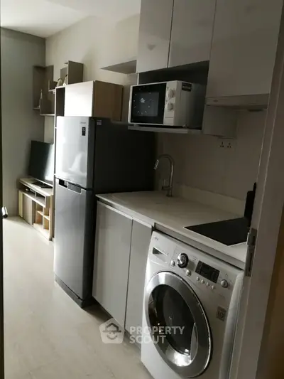 Modern compact kitchen with appliances including fridge, microwave, and washing machine in sleek design.