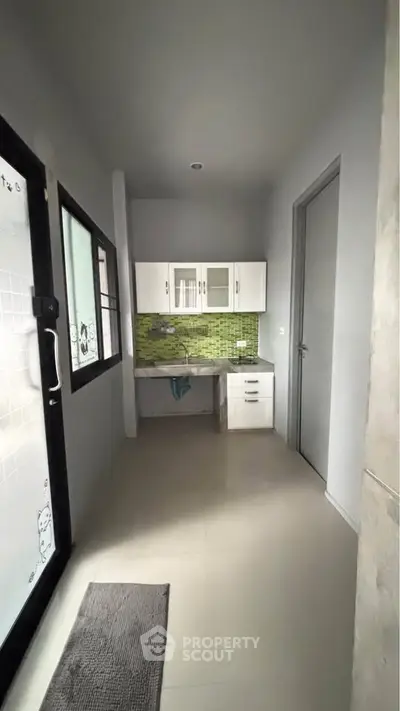Compact kitchen with green backsplash and white cabinets in modern apartment