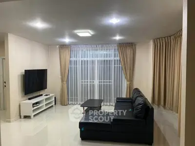 Spacious modern living room with sleek black sofa and large TV, perfect for relaxation and entertainment.