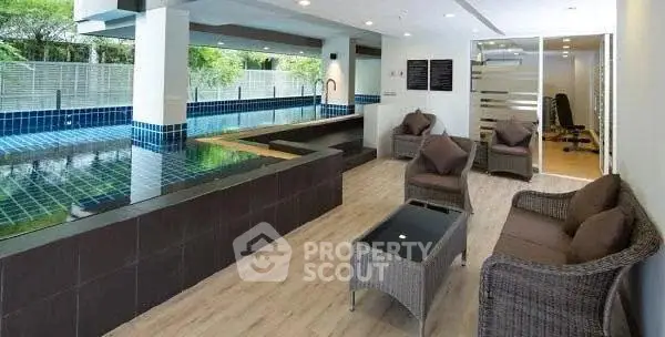 Luxurious indoor pool area with modern seating and fitness room view.