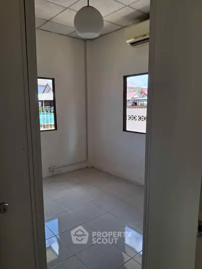 Compact room with tiled floor and two windows, ideal for a small office or study space.