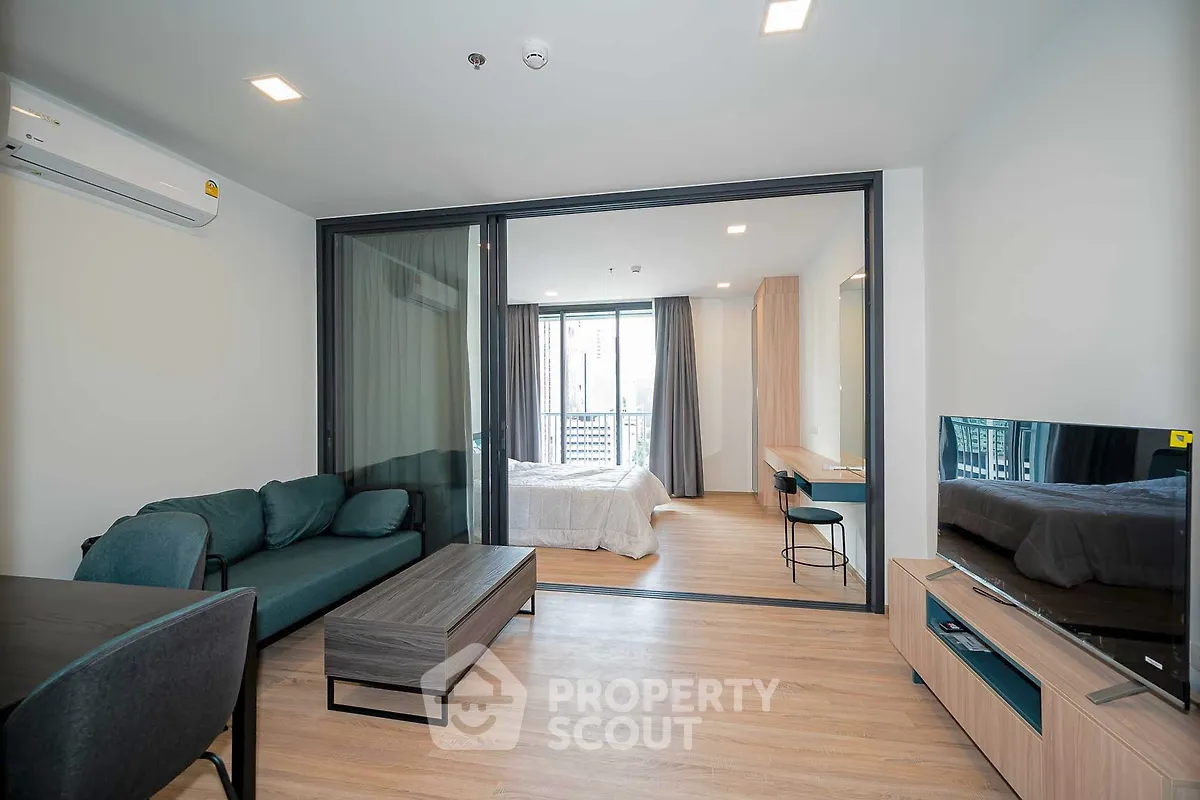 Modern open-plan living room with stylish furniture and bedroom view in a contemporary apartment.