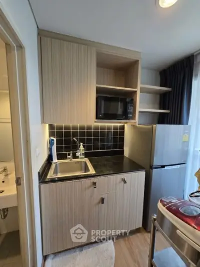 Compact modern kitchen with wooden cabinets, black backsplash, and stainless steel appliances.