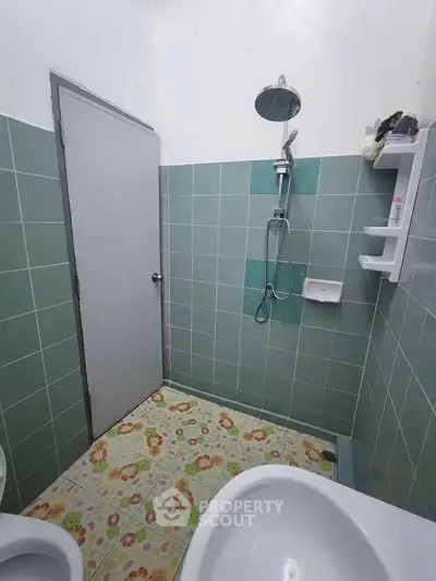 Compact bathroom with green tiles and floral floor design, featuring a shower and modern fixtures.