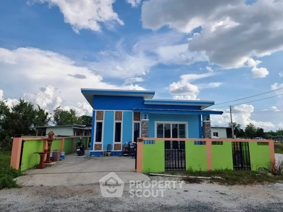 Charming single-story blue house with vibrant accents and spacious driveway under a picturesque sky.