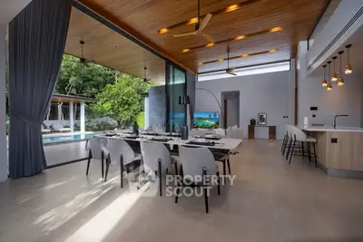 Luxurious open-plan living room with modern dining area and pool view, featuring elegant lighting and wooden ceiling.