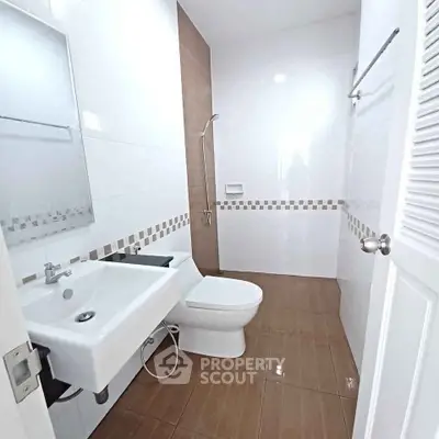 Modern bathroom with sleek design and tiled flooring, featuring a shower and white fixtures.