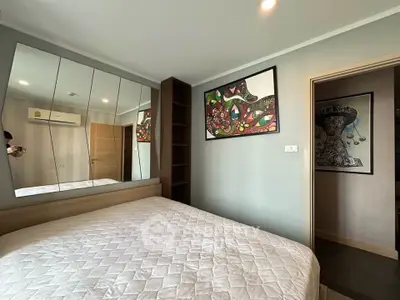 Modern bedroom with stylish decor and mirrored wall, featuring cozy bed and artistic paintings.