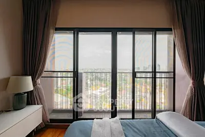 Spacious bedroom with stunning city view from large windows and elegant decor.