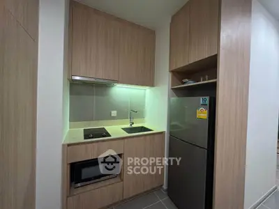 Modern compact kitchen with sleek wooden cabinetry and built-in appliances in a stylish apartment.