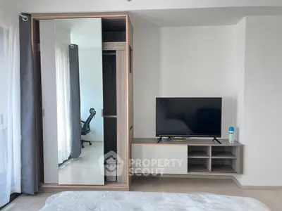 Modern bedroom with sleek wardrobe and TV unit, featuring a stylish chair and natural light.