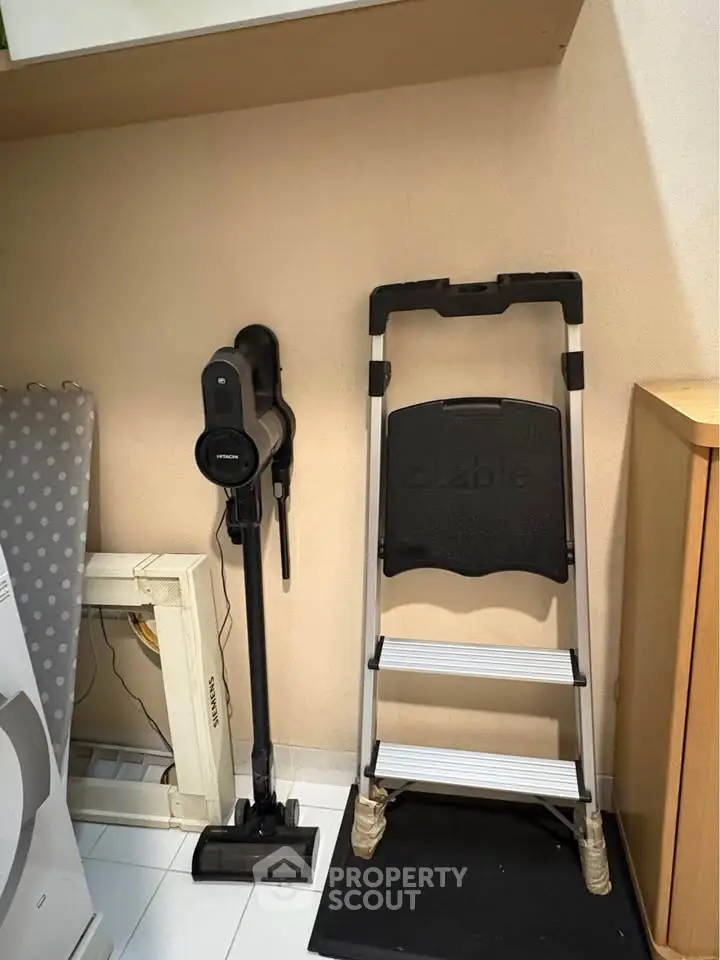 Compact storage area with vacuum cleaner and step ladder, ideal for organized living spaces.