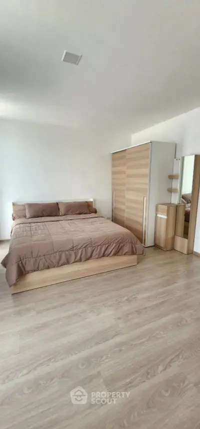 Spacious modern bedroom with wooden flooring and minimalist furniture