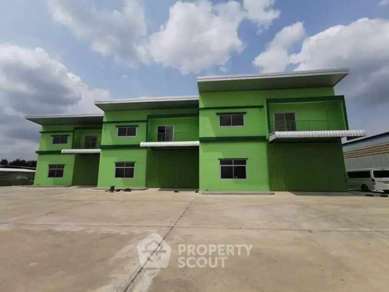 Modern green industrial building with spacious exterior and clear sky view.