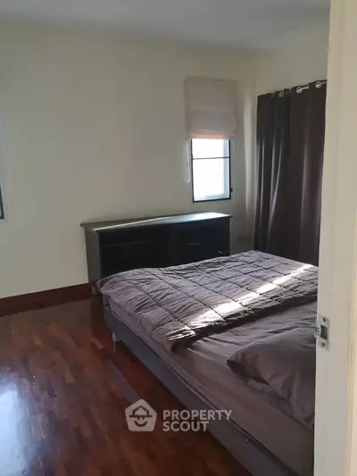 Spacious bedroom with wooden flooring and large windows for natural light.