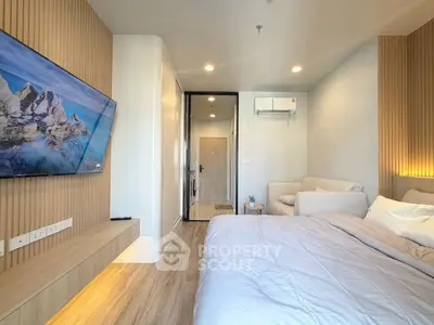 Modern bedroom with cozy seating area and wall-mounted TV, featuring elegant wood paneling and soft lighting.