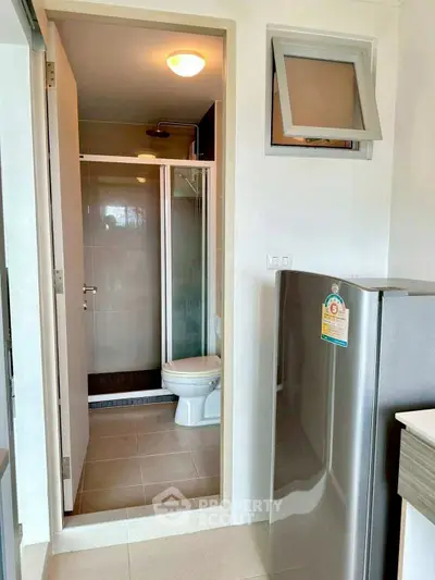 Compact bathroom with shower and adjacent kitchen area featuring a modern fridge.