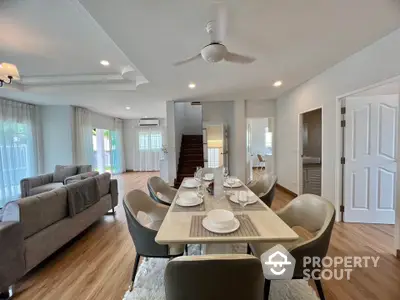 Spacious open-plan living and dining area with modern decor and natural light, featuring elegant furniture and wooden flooring.