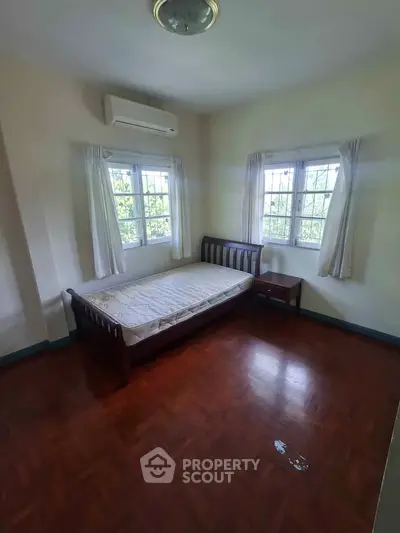 Cozy bedroom with wooden flooring and natural light from two windows.