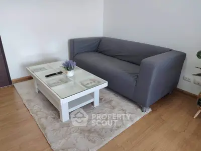 Cozy living room with modern gray sofa and elegant glass coffee table on plush rug.