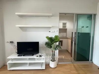 Modern living room with TV stand, open kitchen view, and sliding glass door.