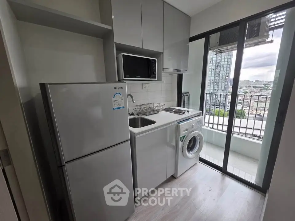 Modern kitchen with balcony view, featuring sleek appliances and ample storage in a compact space.