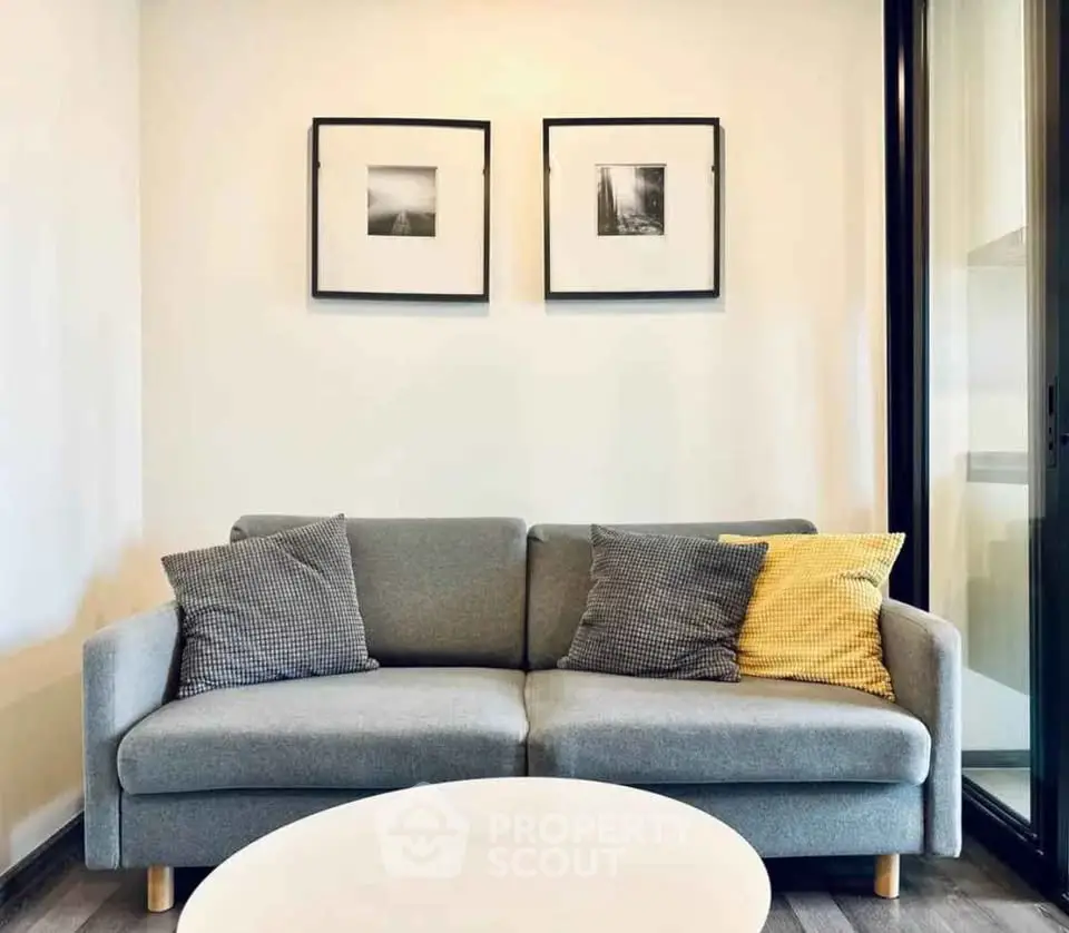 Modern living room with stylish gray sofa and decorative pillows, framed art on wall, and sleek round coffee table.