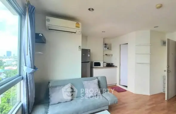 Modern living room with air conditioning and city view, featuring cozy sofa and compact kitchen area.