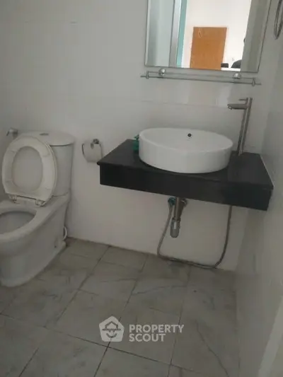 Modern bathroom with sleek sink and toilet, featuring minimalist design and neutral tiles.