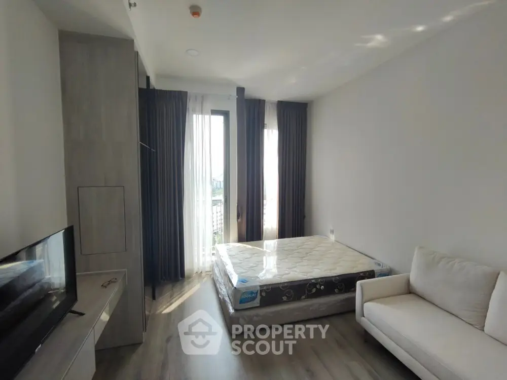 Modern bedroom with natural light, featuring a cozy bed, stylish sofa, and sleek flooring.