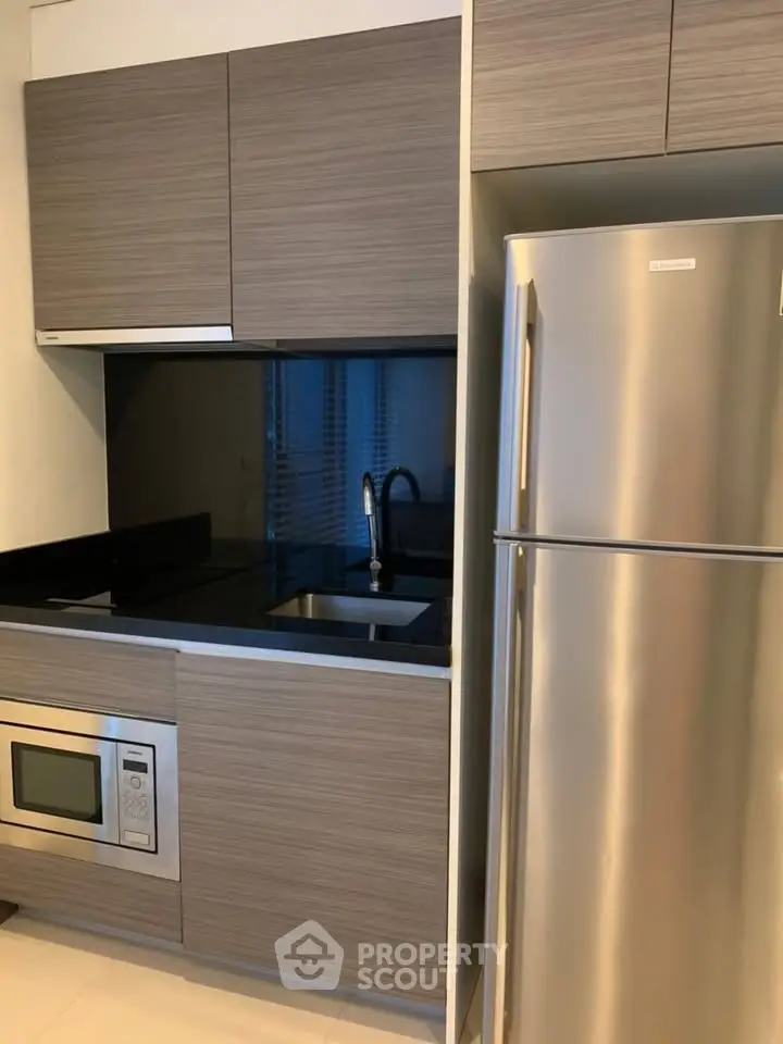 Modern kitchen with sleek cabinetry, stainless steel fridge, and built-in microwave oven.