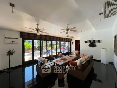 Spacious living room with large windows and garden view, featuring modern furniture and ceiling fans.
