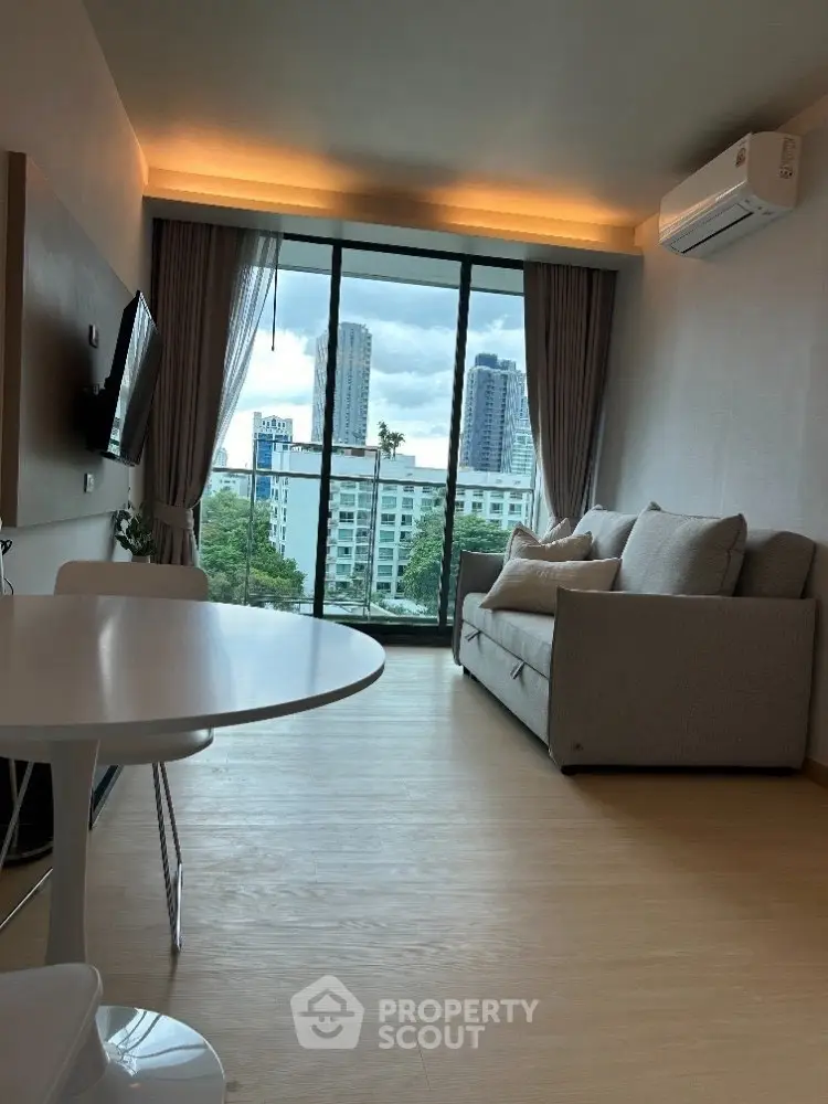 Modern living room with city view, featuring cozy sofa and large windows for natural light.