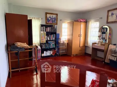 Spacious bedroom with wooden flooring and ample natural light, featuring a bookshelf and vanity area.