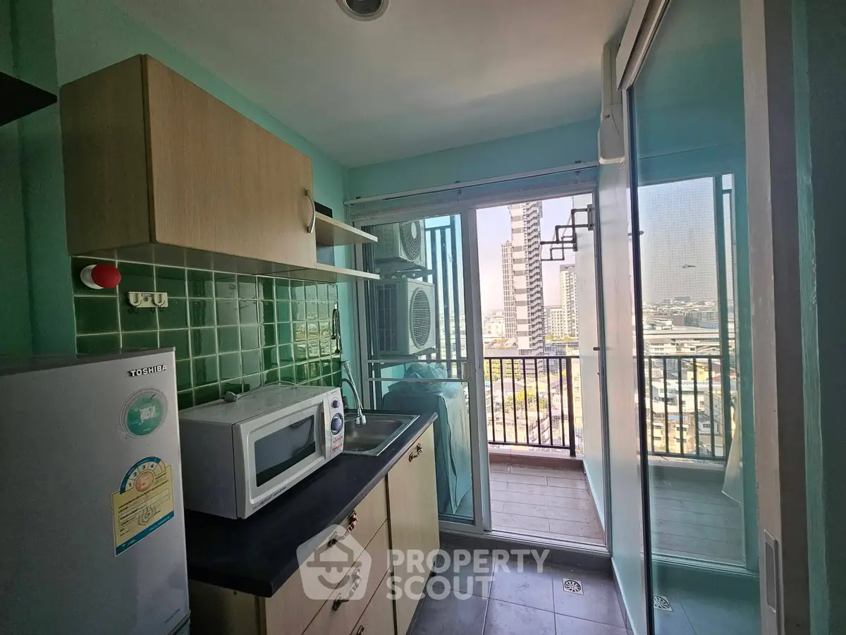 Modern kitchen with balcony view, featuring microwave and compact fridge in a cozy apartment setting.