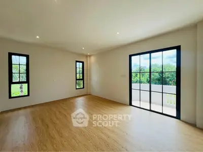 Spacious empty room with large windows and wooden flooring, offering abundant natural light and serene views.