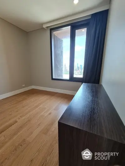 Spacious bedroom with wooden flooring and city view window in modern apartment.