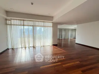 Spacious empty living room with hardwood floors and large windows offering natural light.