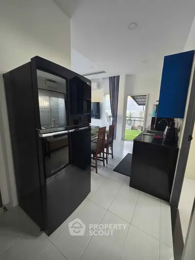 Modern kitchen with sleek black appliances and open layout leading to dining area and balcony.