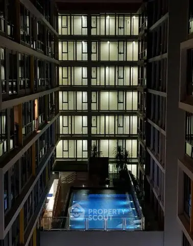 Modern apartment building with illuminated windows and a central pool at night.