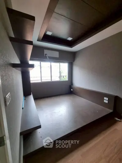 Modern bedroom with built-in wooden platform and shelves, featuring large window for natural light.