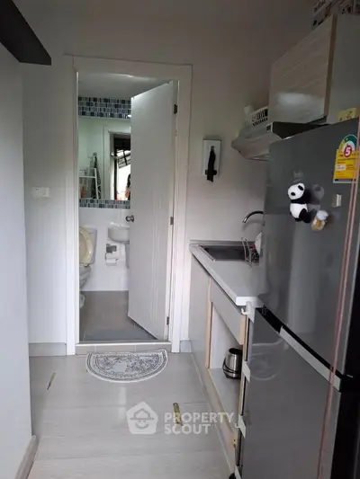 Compact kitchen with modern fridge and bathroom view in cozy apartment