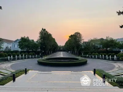 Luxurious estate entrance with manicured gardens and elegant fountain at sunset