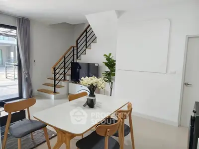 Modern dining area with stylish furniture and staircase in a bright, open-plan home interior.