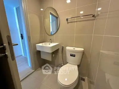 Modern bathroom with sleek fixtures and neutral tiles, featuring a round mirror and compact sink.